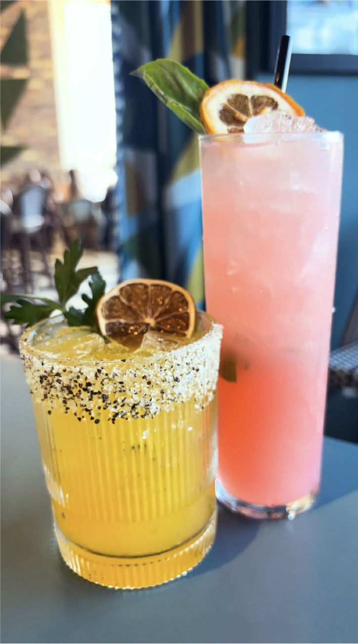 A salted yellow cocktail and a tall pink cocktail on a table at Candle Bar